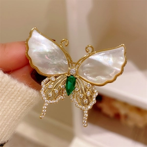 Macro view of butterfly brooch with white shell wings and emerald green gemstone