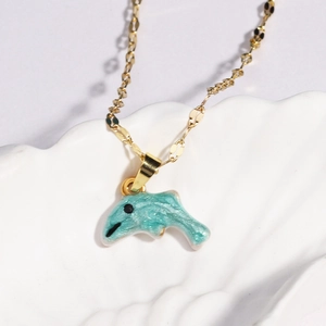 Golden necklace with blue dolphin ocean pendant on a white textured shell background