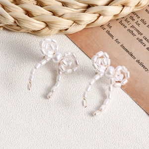 Close-up of handmade woven pearl bow earrings with vintage aesthetic on white texture