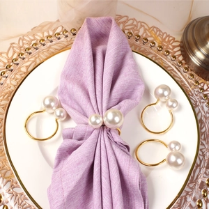 Detail of elegant gold metal napkin rings with pearls on purple linen and gold-rimmed plates