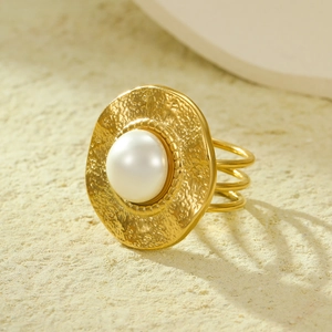 18K gold textured round ring with a large pearl center on a beige stone surface