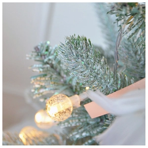 Close-up of warm LED globe lights on snow-flocked pine branches with elegant ribbons