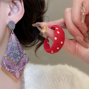 Detail of vintage geometric earrings and red polka dot C-ring with gold fish accent