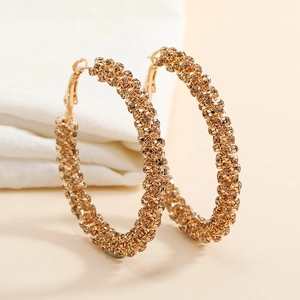 Macro detail of gold large hoop earrings with sparkling rhinestones on beige fabric