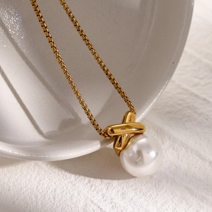 Detail shot of a large white pearl pendant with a golden X-shaped clasp on a necklace