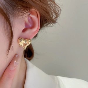 Détail de puce d'oreille cœur doré avec texture martelée sur lobe d'oreille