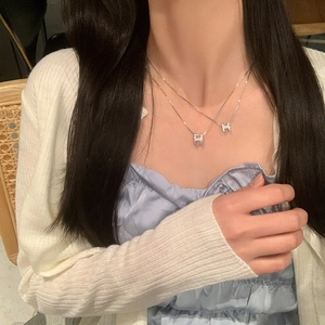 Close-up of double-layer silver necklace with sparkling zircon H-letter pendants on model