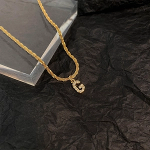 Gros plan du pendentif lettre G doré orné de zircons blancs sur une chaîne tissée élégante