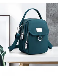 Detail of teal nylon crossbody bag with multi-layer zippers and woven shoulder strap