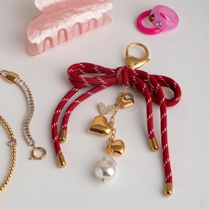 Close-up of red ribbon bow bag charm with gold hearts and a large baroque pearl