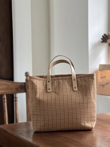Detail of vintage brown plaid canvas tote featuring leather handles and metal rivets