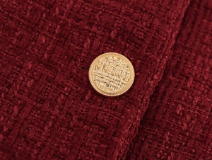 Detail of burgundy tweed fabric texture with an embossed gold button on a dress