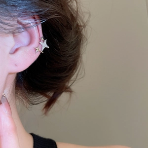 Detail of star-shaped ear cuff with zircons worn by model in a soft lighting