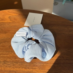 Close-up of light blue fabric scrunchie with button detail on dark wooden desk