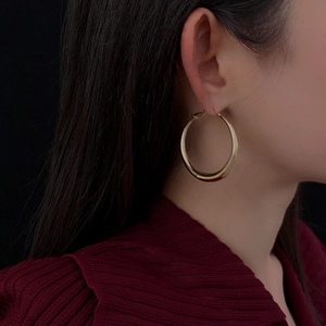 Close-up of model wearing gold hoop earrings with a polished finish on black background