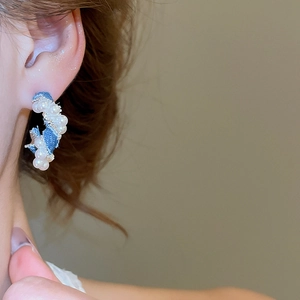 Detail of C-shaped hoop earring featuring blue denim fabric and white pearl accents