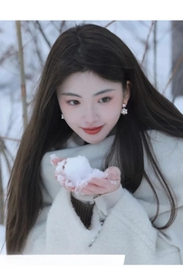 Close-up of 14k gold plated snowflake earrings worn by model in a snowy outdoor setting