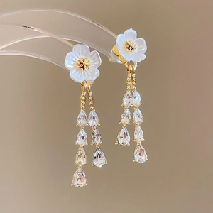 Elegant gold flower tassel earrings with sparkling white crystals on a luxury display stand