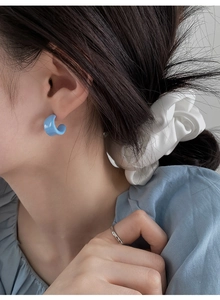 Close-up of a blue resin C-shaped earring worn by a model in soft daylight