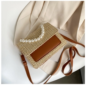 Detail of woven straw handbag featuring pearl top handle and brown leather flap accents