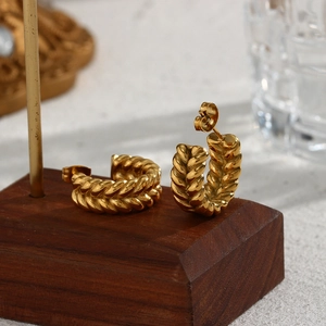 Macro shot of gold-plated twisted wheat pattern C-shaped earrings on a wooden base