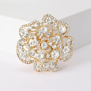 Macro shot of gold rose brooch encrusted with sparkling crystals on white pedestal