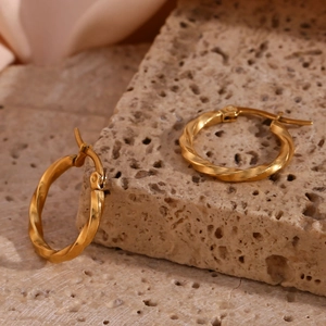 Detailed close-up of 18K gold plated twisted hoop earrings on beige stone and pink silk