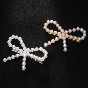 Close-up of gold and silver bow hair clips with pearls on a dark textured surface