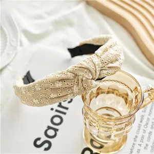 Detail of beige knotted headband with white floral embroidery on cotton linen fabric