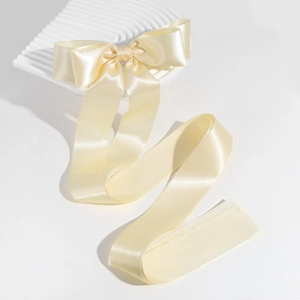 Detail of elegant cream satin ribbon bow hair clip on a wavy white decorative surface