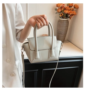 Close-up of light gray leather handbag with trapezoidal structure and gold hardware