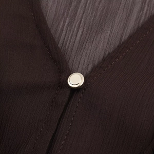 Macro detail of silver metal button on chocolate brown chiffon v-neck dress fabric