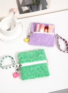 Close-up of soft plush mini cosmetic bags in purple and green with heart charms