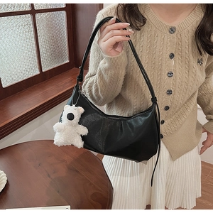 Detail of black PU leather shoulder bag with a cute white plush bear pendant on strap