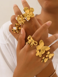Close-up of 18k gold butterfly and flower rings with pearls worn on model hand