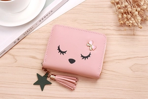 Pink PU leather short wallet featuring cartoon eyelash print and tassel charm on a table