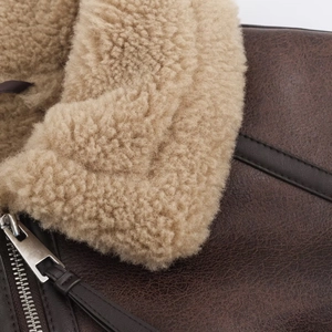 Detail of dark brown leather jacket featuring plush beige faux fur collar and metal zipper