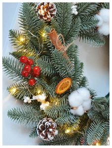 Detail of Christmas wreath with pine cones, red berries, cotton and warm LED lights