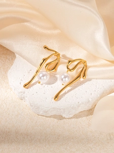Detail of elegant gold twist earrings with hanging white pearls on a silk background