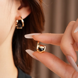Detailed view of a gold geometric D-shaped earring featuring a black square stone inlay