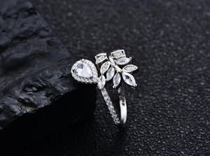 Macro shot of silver leaf-shaped ring with pear-cut zircon stones on black rock texture