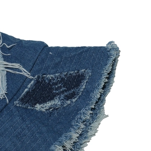 Detailed close-up of blue denim bucket hat with distressed frayed edges and patchwork design