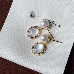 Dettaglio orecchini vintage in oro con perle e pietra di conchiglia bianca su scheda