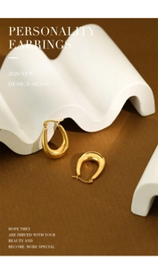 Polished gold U-shaped geometric hoop earrings displayed on an artistic wave prop