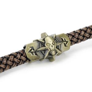 Detail of a brown braided leather bracelet featuring a bronze skull and cross charm
