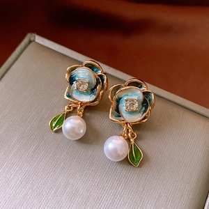 Detail of gold floral earrings with turquoise enamel petals and hanging white pearl