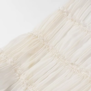 Dettaglio in primo piano di chiffon bianco a pieghe e pizzo su un set gonna lunga