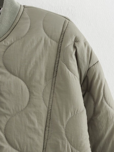 Detailed view of olive green quilted jacket featuring wavy patterns and ribbed stand collar