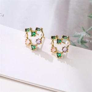 Macro detail of gold heart earrings with colored zircons and white pearls on a white card