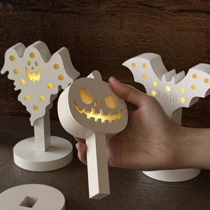 Macro shot of Halloween ghost, pumpkin, and bat silhouette lights on a rustic wood surface